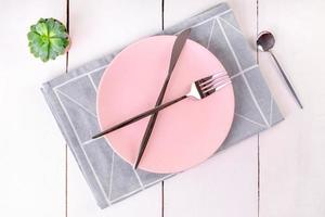 Sirviendo plato rosa vacío con cuchillo cruzado y tenedores en una servilleta de lino doblada con patrón geométrico foto