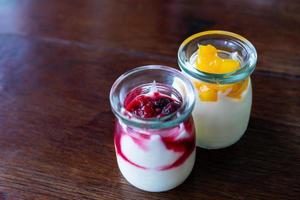 Yogur griego con bayas y mango en frascos de vidrio sobre fondo de madera foto