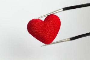 Tweezers holding decorative heart on a white background. photo