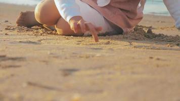 zorgeloos onherkenbaar meisje dat een hartvorm tekent op het natte zand bij exotische zonsondergang video