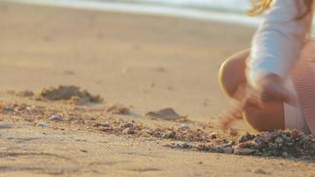 Carefree unrecognizable girl places seashells in a drawn heart shape on wet sand at exotic sunset video