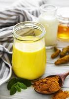 Yellow turmeric latte drink. Golden milk with cinnamon, turmeric, ginger  and honey over white wooden background. photo