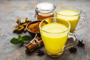 Yellow turmeric latte drink. Golden milk with cinnamon, turmeric, ginger  and honey over concrete background. photo