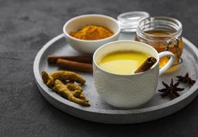 Yellow turmeric latte drink. Golden milk with cinnamon, turmeric, ginger  and honey over black concrete background. photo