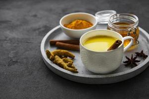 Yellow turmeric latte drink. Golden milk with cinnamon, turmeric, ginger  and honey over black concrete background. photo