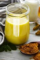 Yellow turmeric latte drink. Golden milk with cinnamon, turmeric, ginger  and honey over white wooden background. photo
