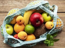 Mesh shopping bag with organic fruits on wooden background. Flat lay, top view. Zero waste, plastic free concept.  Summer fruits. photo