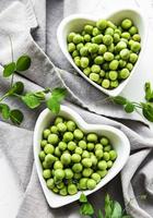 Green peas in heart shaped bowls on a fabric background photo