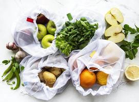 Fruits and summer vegetables in reusable eco friendly mesh bags on marble background. Zero waste shopping. Ecological concept. photo