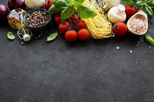 Dieta mediterránea saludable, ingredientes para comida italiana, espaguetis, tomates, albahaca, aceite de oliva, ajo, pimientos sobre fondo negro foto