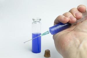 mano que sostiene el tubo de ensayo con líquido azul y una jeringa. foto