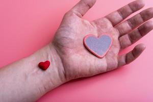 man holds a red heart in his palms on a pink background photo