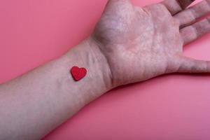 Heart on the wrist of a man's hand on a pink background.
