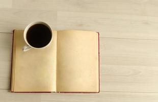 a cup of coffee and an open book on white wooden background.Top view,space for text. photo