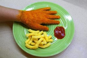 Hand covered with fried bread crumbs, crispy appearance looks like schnitzel, is placed on a green plate with fries and ketchup