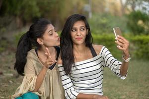 Two beautiful female friends taking selfie with smartphone in outdoors. photo