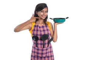 Young Indian woman holding kitchen utensil spoon, stapula, ladle, and pan, etc. on a white background photo