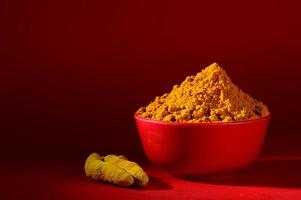 Dry Turmeric powder and roots or barks in red bowl on red background photo