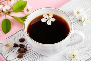 Strong espresso coffee on a white wooden tray. Spring flowers of an apple tree on a pink background. photo