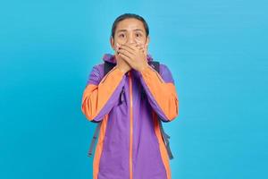 Shocked young Asian man covering mouth with hand on blue background