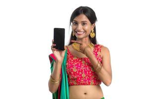 Young Indian traditional girl using a mobile phone or smartphone and showing blank screen smart phone on white background photo