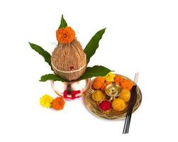 kalash de cobre con hoja de coco y mango y pooja thali con diya, kumkum y dulces con decoración floral sobre fondo blanco. esencial en puja hindú. foto