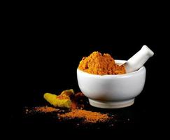 Turmeric powder in mortar with pestle and roots or barks on black background photo