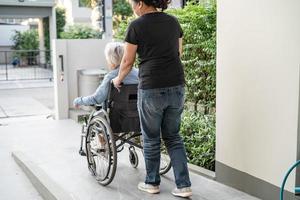 Caregiver help and care Asian senior or elderly old lady woman patient sitting in wheelchair on ramp at nursing hospital, healthy strong medical concept photo