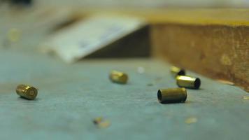 Empty pistol bullet shells dropping and impacting wooden table in a shooting range video