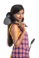 Young Indian woman holding kitchen utensil spoon, stapula, ladle, and pan, etc. on a white background photo