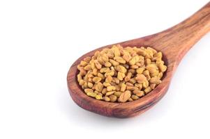 Fenugreek seeds in wooden spoon isolated on white background photo