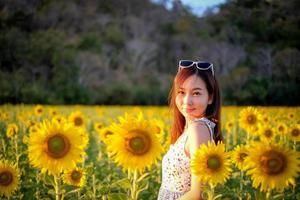 feliz alegre niña asiática con girasol disfrutando de la naturaleza y sonrisa en verano en el campo de girasol. foto