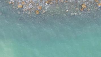 bovenaanzicht, kleine zeegolven blazen zachtjes op het wateroppervlak. de rotsen zijn omgeven door zeewater. video