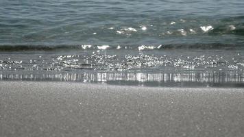 les vagues de l'océan lavent doucement la plage. la lumière du soleil frappe la surface de l'eau. video