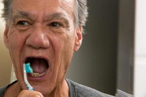 Mature Man Brushing his teeth with a Worn out Tooth Brush photo