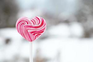 Heart shaped pink lollipop. Caramel candy on stick. Sweet gift for valentines day. photo