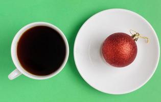 Top view, A cup of black coffee and red Christmas ball on the plate on green background.Christmas coffee. photo