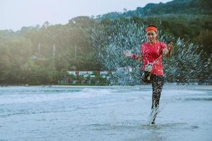 asian woman jogging workout on the beach in the morning. Relax with the beach. fun and happy with playing, jumping, kicking the sea. in summer photo