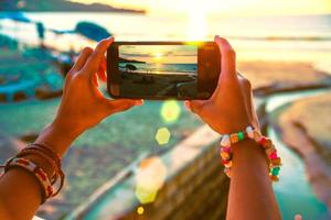 naturaleza de viaje de mujer asiática. viajar relajarse. utilizar el teléfono celular para tomar fotografías de la puesta de sol en la playa. en el verano