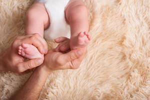 Dad holds in his hands a small baby foots. Small legs of a newborn baby in large hands of dad. Baby foot massage photo