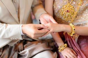 La novia y el novio poniendo el anillo de bodas en el dedo, ceremonia de compromiso de boda tailandesa foto