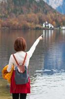 Asian tourist traveller girl from back standing pointing finger at Hallstatt lake Austria in autumn, freedom peaceful relax concept photo