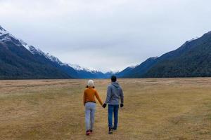 Joven pareja asiática tomados de la mano caminando hacia la montaña eglinton valley parque nacional de Fiordland Nueva Zelanda foto