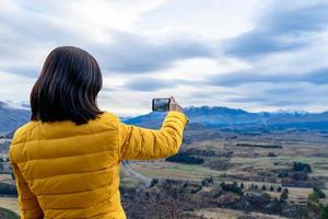 Mujer turista asiática tomando fotos con un teléfono móvil en Queenstown, Isla del Sur, Nueva Zelanda