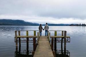 joven pareja asiática tomados de la mano en el puente del lago te anau nueva zelanda foto