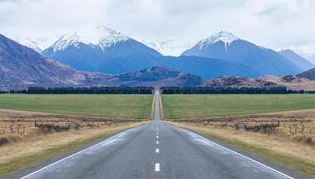 Panoramic view of long straight open icy road leading towards mountains in south island New Zealand