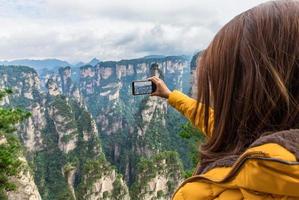 Chica turista asiática tomando una foto con un teléfono inteligente en el parque forestal nacional de Zhangjiajie, sitio del patrimonio mundial de la unesco, Wulingyuan, Hunan, China