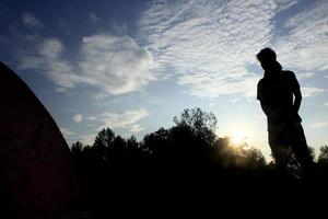 silhouette of a climber with a tent on bright blue sky background photo