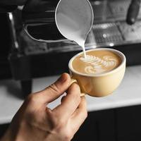 close up hand pouring milk coffee cup