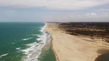 Imágenes de drones aéreos volando sobre una playa con dunas y cielo nublado video